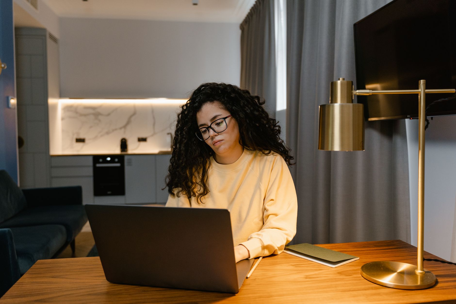 A person working from a home desk, with a laptop, a separate screen and a notebook